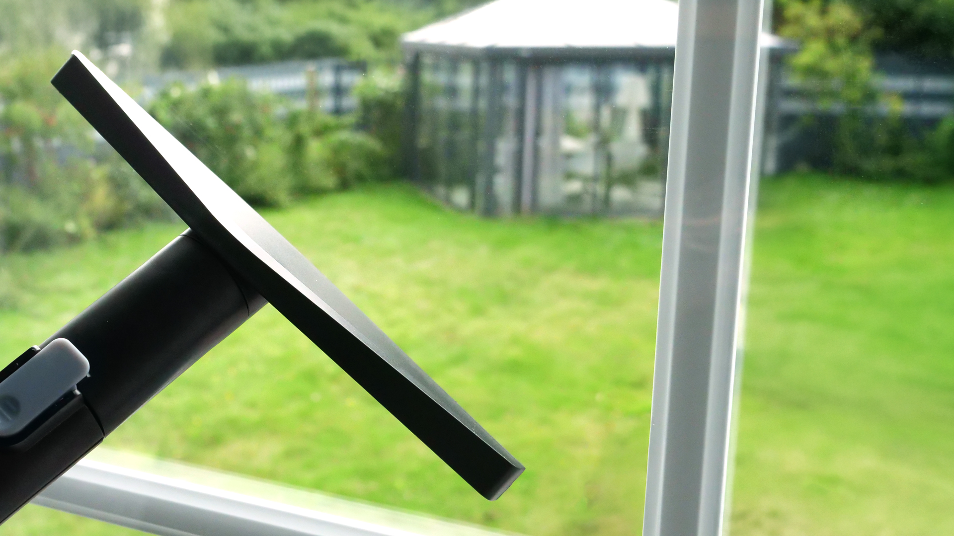 Eine breite Düse gleitet über eine Fensterscheibe, hinter der ein Garten sichtbar ist.